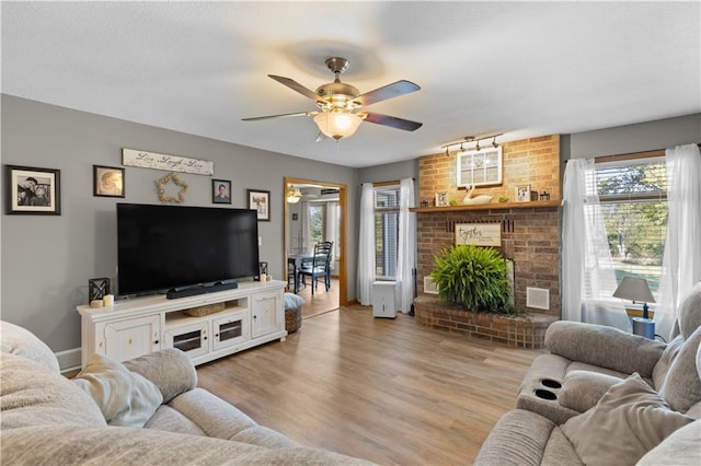 living room featuring a brick fireplace, ceiling fan, and light hardwood / wood-style flooring