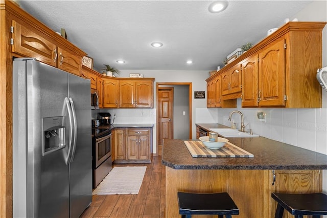 kitchen with appliances with stainless steel finishes, a breakfast bar area, sink, and dark hardwood / wood-style floors