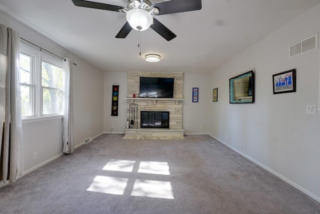 unfurnished living room with ceiling fan, a stone fireplace, and light colored carpet