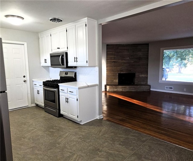 kitchen featuring tasteful backsplash, a stone fireplace, dark hardwood / wood-style flooring, white cabinets, and appliances with stainless steel finishes