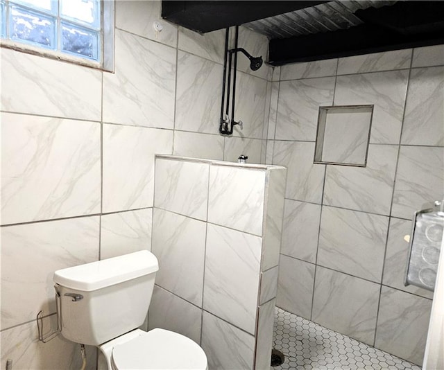 bathroom with a tile shower, tile walls, and toilet