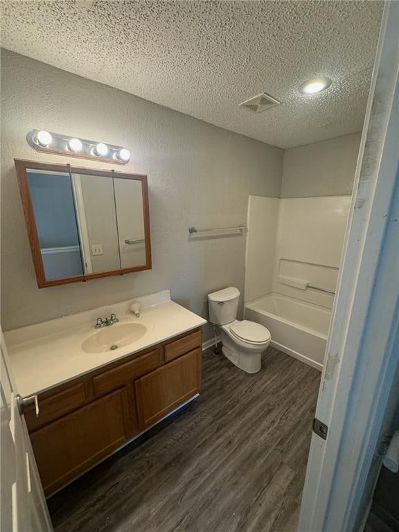 full bathroom with bathtub / shower combination, a textured ceiling, wood-type flooring, toilet, and vanity