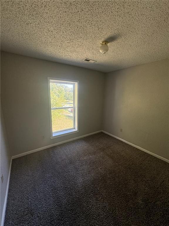 unfurnished room with a textured ceiling and dark colored carpet