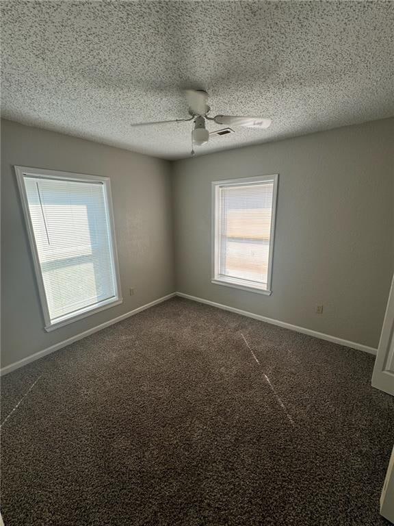 empty room with dark carpet, a textured ceiling, and ceiling fan