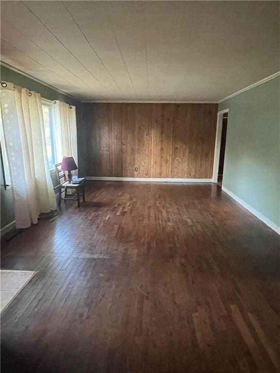 empty room featuring dark wood-type flooring, wood walls, and ornamental molding