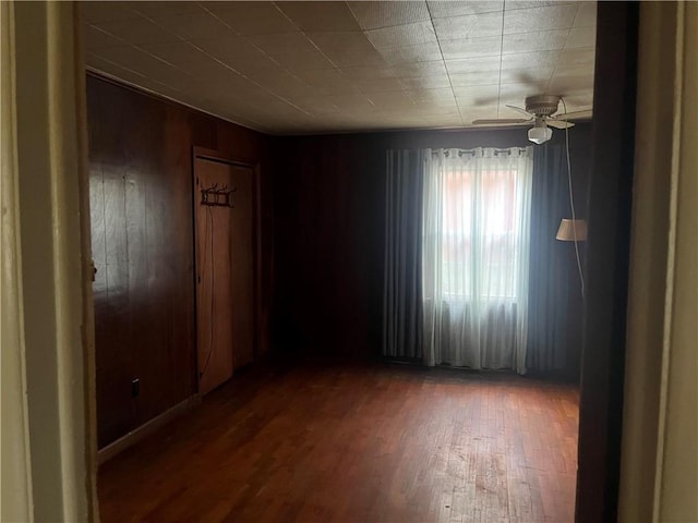 empty room featuring ceiling fan, wooden walls, and hardwood / wood-style floors