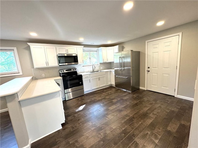 kitchen featuring appliances with stainless steel finishes, sink, kitchen peninsula, white cabinets, and dark hardwood / wood-style floors