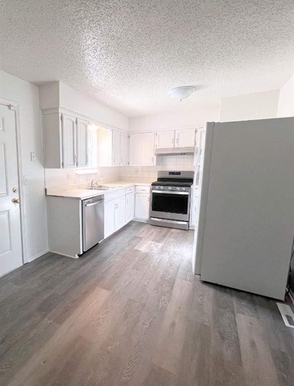 kitchen featuring decorative backsplash, hardwood / wood-style flooring, white cabinetry, appliances with stainless steel finishes, and a textured ceiling