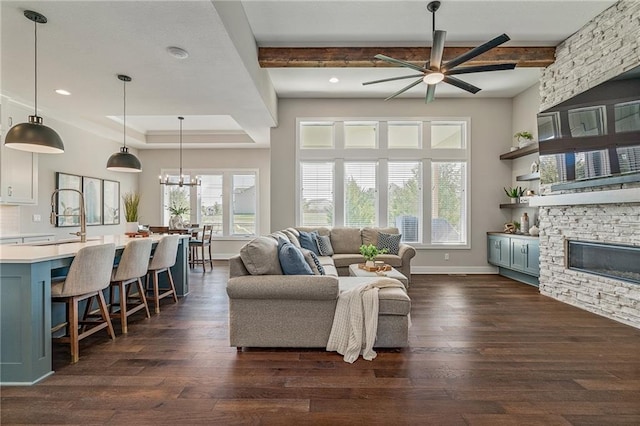 living room featuring a stone fireplace, ceiling fan with notable chandelier, dark hardwood / wood-style floors, and beam ceiling