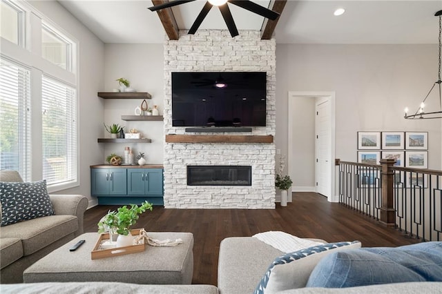 living room featuring ceiling fan with notable chandelier, beamed ceiling, a fireplace, and dark wood-type flooring