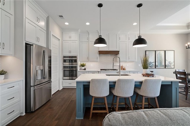 kitchen featuring decorative light fixtures, an island with sink, appliances with stainless steel finishes, and dark wood-type flooring