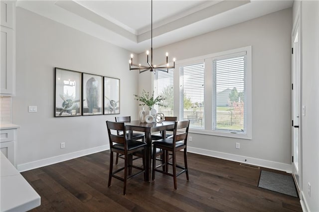 dining space with a chandelier, a raised ceiling, dark wood-type flooring, and crown molding