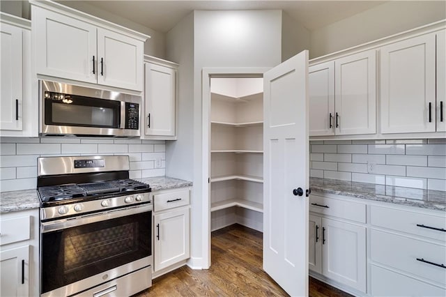 kitchen featuring white cabinets, appliances with stainless steel finishes, wood finished floors, light stone countertops, and backsplash