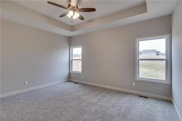 unfurnished room with ceiling fan, carpet floors, visible vents, baseboards, and a tray ceiling