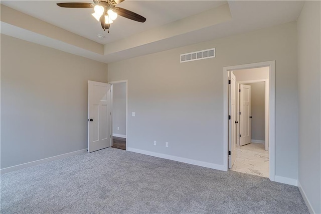 spare room featuring carpet floors, a raised ceiling, visible vents, and baseboards