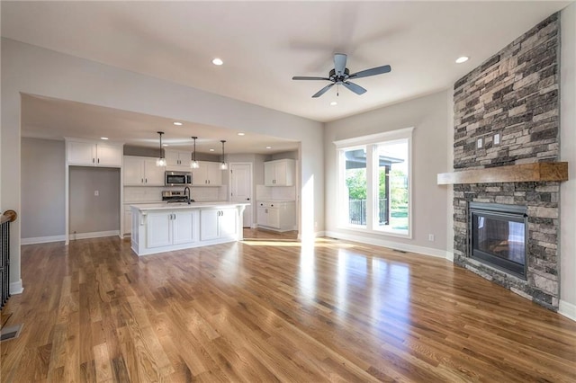 unfurnished living room featuring light hardwood / wood-style floors, a stone fireplace, and ceiling fan