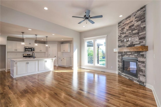 unfurnished living room featuring sink, ceiling fan, a stone fireplace, and light hardwood / wood-style flooring