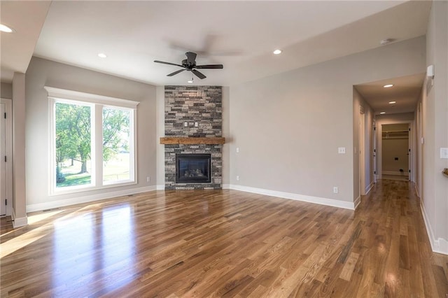 unfurnished living room featuring a stone fireplace, wood-type flooring, and ceiling fan