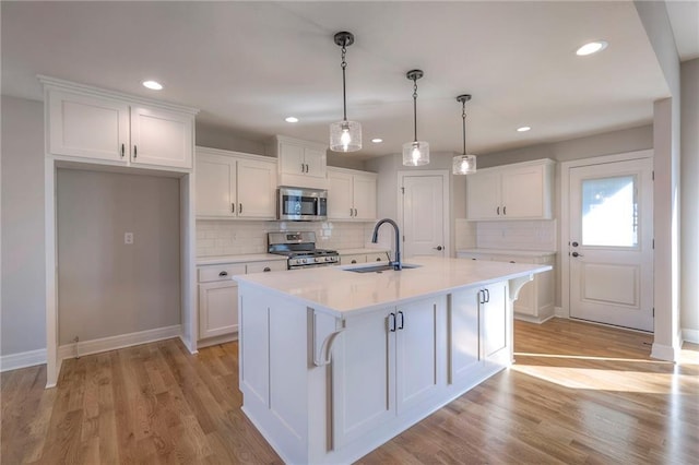 kitchen with a kitchen island with sink, sink, white cabinets, appliances with stainless steel finishes, and light hardwood / wood-style floors