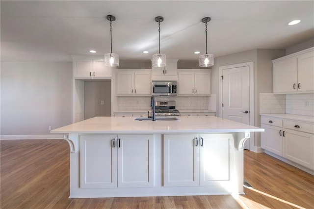 kitchen featuring stainless steel appliances, a center island with sink, and light wood-type flooring