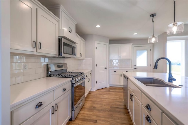 kitchen featuring light wood-type flooring, backsplash, white cabinetry, stainless steel appliances, and decorative light fixtures