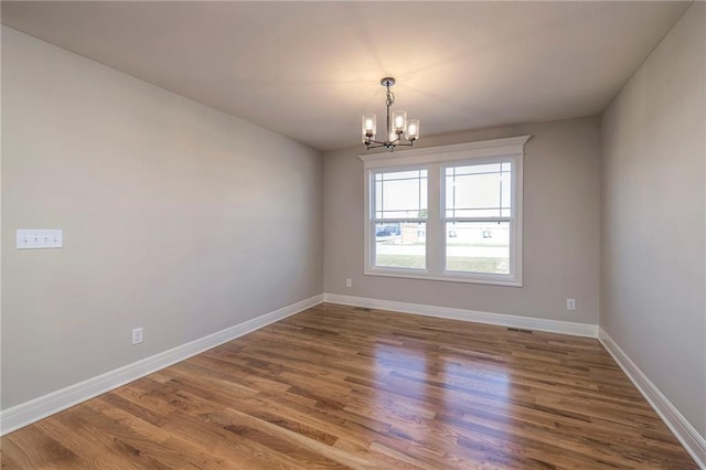 empty room featuring a chandelier and hardwood / wood-style flooring