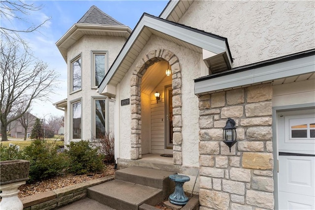 property entrance featuring stone siding, roof with shingles, and stucco siding