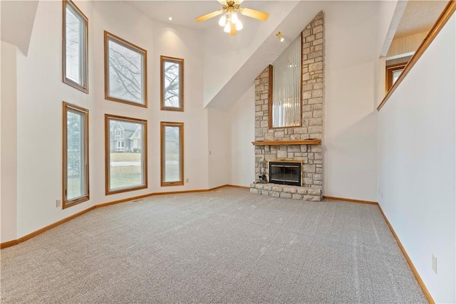 unfurnished living room with carpet floors, a towering ceiling, a ceiling fan, a stone fireplace, and baseboards