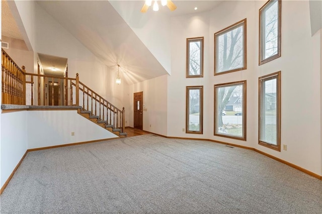 unfurnished living room with carpet floors, visible vents, a towering ceiling, baseboards, and stairs