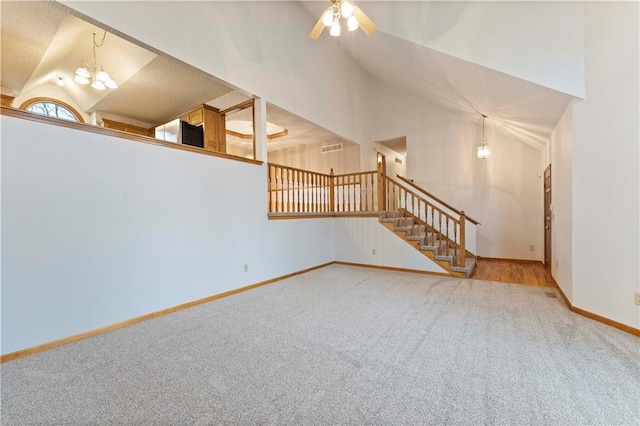 carpeted empty room with ceiling fan with notable chandelier, visible vents, baseboards, vaulted ceiling, and stairway