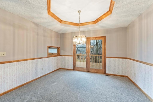 spare room featuring a notable chandelier, a raised ceiling, carpet flooring, a textured ceiling, and wallpapered walls