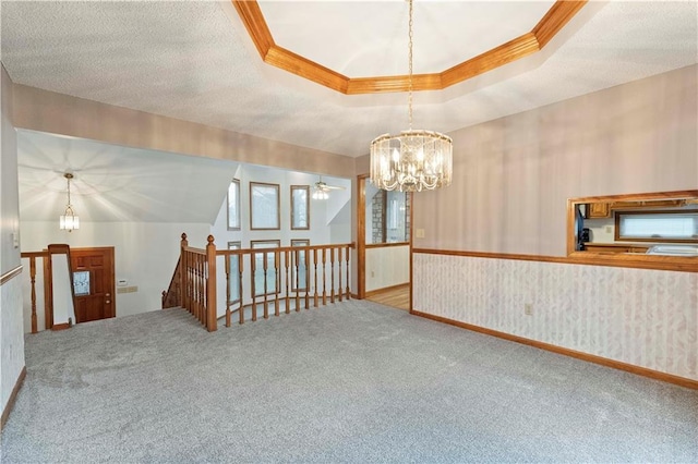 carpeted empty room featuring crown molding, a raised ceiling, wallpapered walls, a textured ceiling, and ceiling fan with notable chandelier