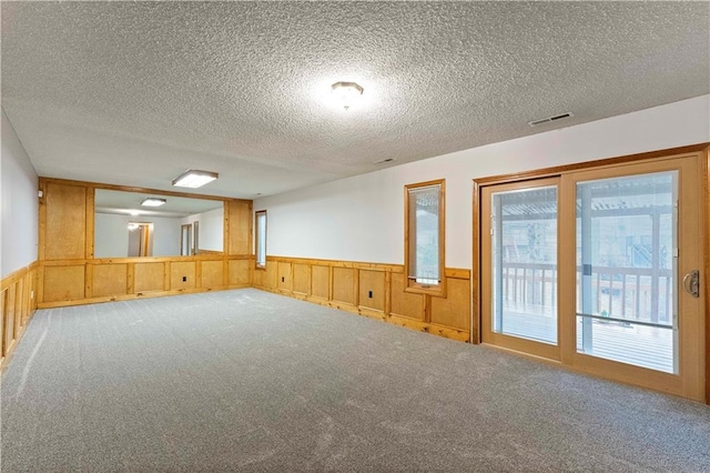 empty room with a wainscoted wall, carpet floors, a textured ceiling, and visible vents