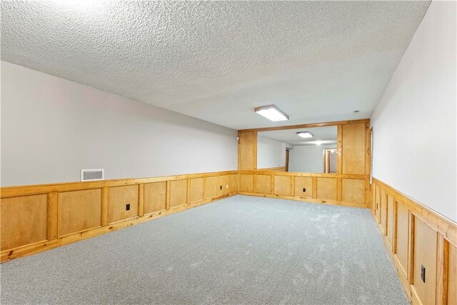 empty room featuring a textured ceiling, light colored carpet, wood walls, visible vents, and wainscoting