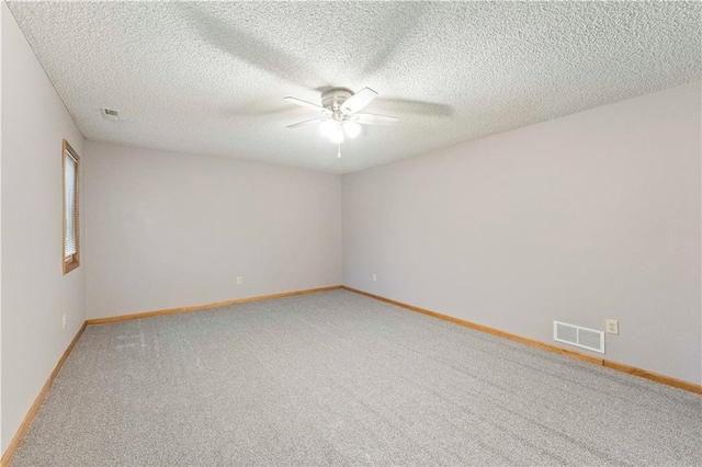 spare room with a textured ceiling, light carpet, visible vents, baseboards, and a ceiling fan