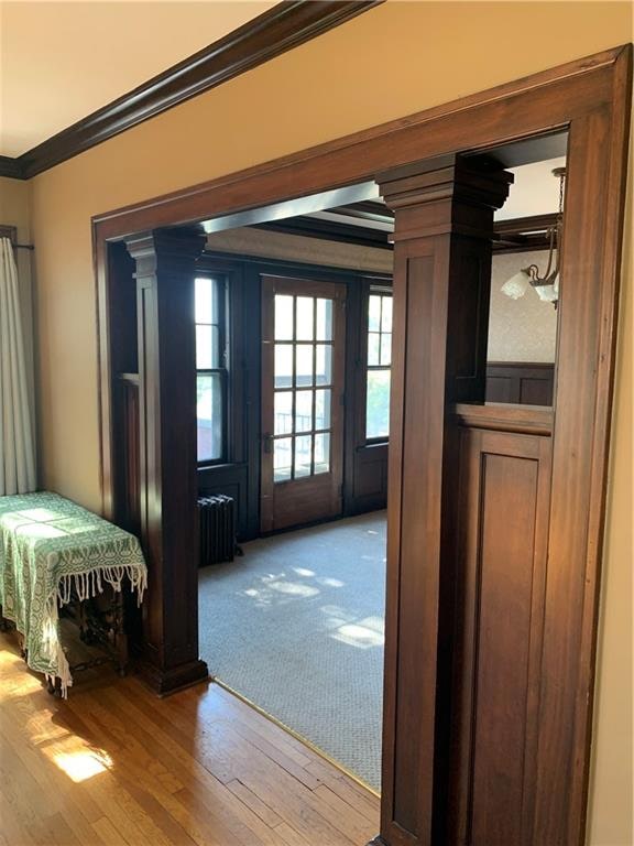 hallway featuring hardwood / wood-style flooring, crown molding, decorative columns, and radiator heating unit