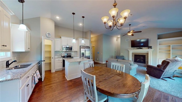 dining area with lofted ceiling, sink, a brick fireplace, dark hardwood / wood-style floors, and ceiling fan with notable chandelier