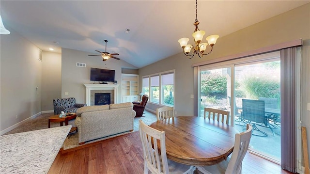 dining space with ceiling fan with notable chandelier, lofted ceiling, a brick fireplace, and hardwood / wood-style flooring