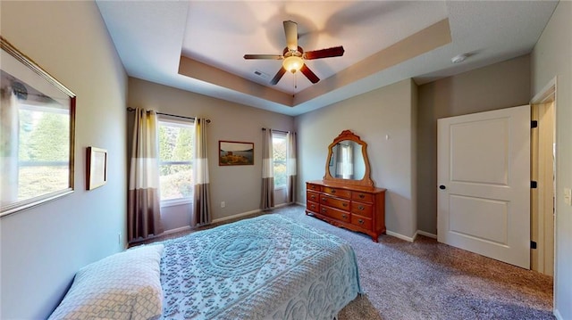 carpeted bedroom featuring ceiling fan and a tray ceiling