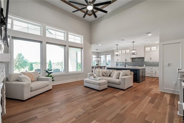 living room with a high ceiling, ceiling fan with notable chandelier, sink, hardwood / wood-style flooring, and a fireplace