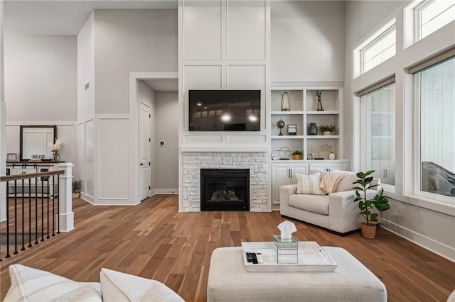 living room with a stone fireplace, built in shelves, and hardwood / wood-style floors