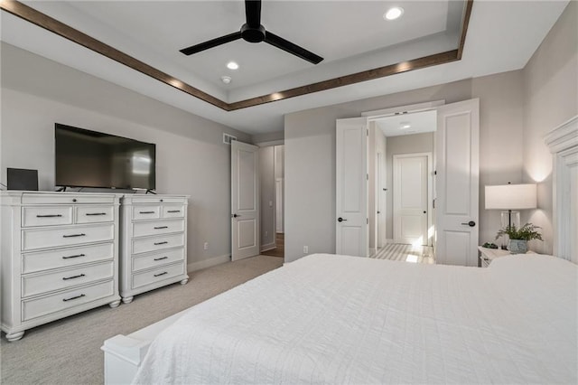 bedroom with a raised ceiling, ceiling fan, and light colored carpet