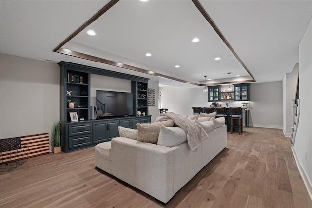 living room with bar area, light hardwood / wood-style flooring, and a tray ceiling