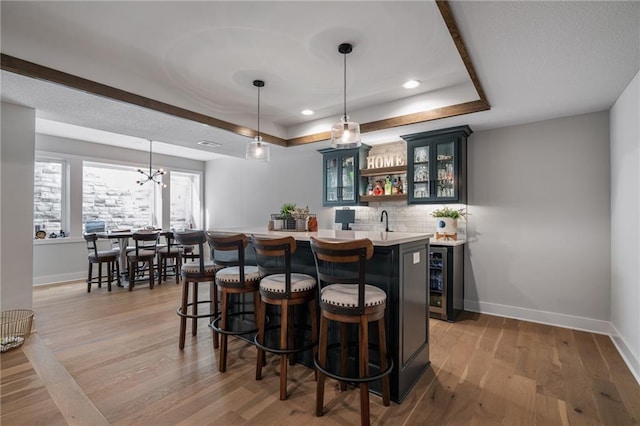 bar with tasteful backsplash, a tray ceiling, beverage cooler, pendant lighting, and light hardwood / wood-style flooring