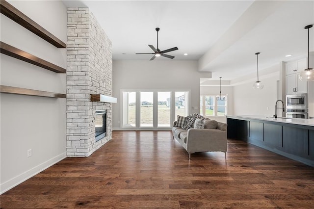 unfurnished living room with ceiling fan with notable chandelier, a stone fireplace, a towering ceiling, and dark wood-type flooring