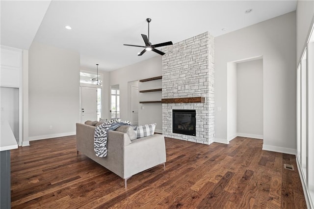 living room with a stone fireplace, ceiling fan with notable chandelier, and dark hardwood / wood-style floors