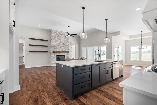 kitchen with dishwashing machine, a center island with sink, a fireplace, and dark hardwood / wood-style flooring