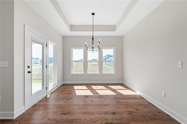 unfurnished dining area featuring a tray ceiling, an inviting chandelier, and dark wood-type flooring