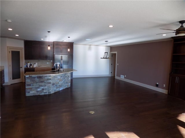 kitchen with stainless steel refrigerator, sink, dark wood-type flooring, pendant lighting, and a kitchen island with sink