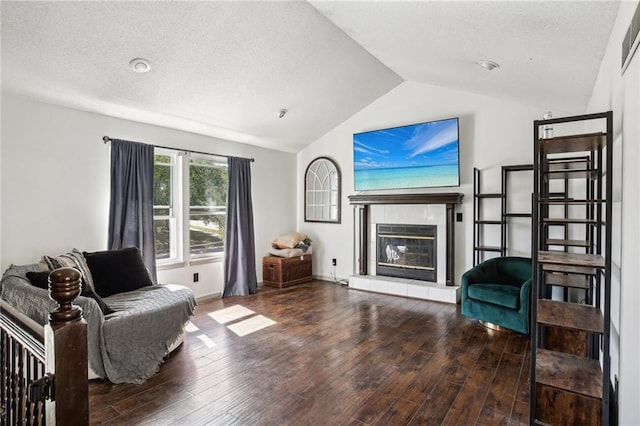 living room featuring a textured ceiling, wood-type flooring, vaulted ceiling, and a tiled fireplace